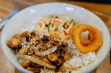 Lezzetli Teriyaki usulü tavuklu pilav kasesi taze salata ve ahşap bir masada gevrek soğan halkası. Yemek blogları için mükemmel.