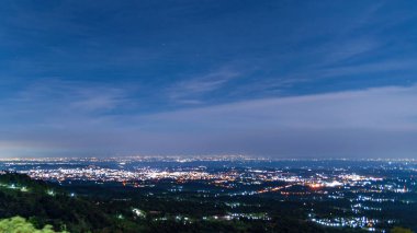 Şehir ışıklarının yamaçtaki ormandan çarpıcı gece manzarası, kentsel ışıltıyı yıldızlı gökyüzünün altında sakin doğal manzarayla harmanlıyor..