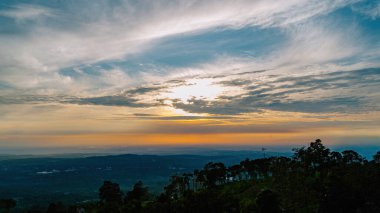 Sisli bir arazide nefes kesici bir gün doğumu, kızgın bir gökyüzü ve yumuşak bulutlar sakin bir atmosfer yaratıyor.