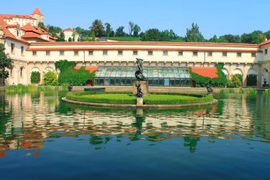 PRAGUE, CZECH REPUBLIC - 27 AĞUSTOS 2018: Wallenstein Garden 'daki bir göldeki yansımanın görüntüsü, heykelleri ve çeşmesi, canlı mavi gökyüzüne ve beyaz bulutlara karşı kırmızı kiremitli çatı. Prag.