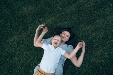 Anne ve oğlu yazın parkta yürürken yeşil çimlerin üzerinde uzanır ve bol bol gülümserler. Çocuk ve anne kollarını açmış birbirlerine sarılıp gülüyorlar. Üst açı, üst açı. Metin için yer