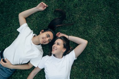 Beyaz tişörtlü gülümseyen iki güzel Avrupalı esmer yaz günü parkta çimlerin üzerinde uzanıp birbirlerine bakarlar. Özgürlük, arkadaşlık, tatil ve eğlence kavramı
