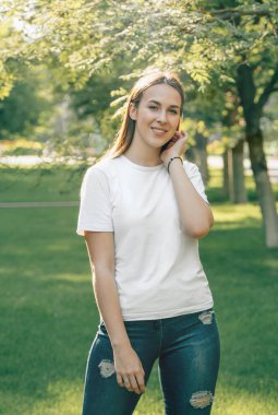 Yeni moda beyaz tişörtlü güzel bir Avrupalı esmerin portresi. Seksi kaygısız beyaz kadın sevinir ve gülümser. Güneşli yaz havasında poz veren kız.