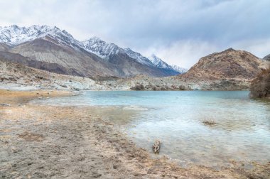 Yarab Tso 'nun manzarası, Hindistan' ın Nubra Vadisi 'ndeki turkuaz mavi göl. Durgun su, arka planda görkemli Himalaya dağlarıyla bulutlu gökyüzünü yansıtırken renkli Budist dua bayrakları ruhani ve kültürel bir dokunuş ekliyor.. 