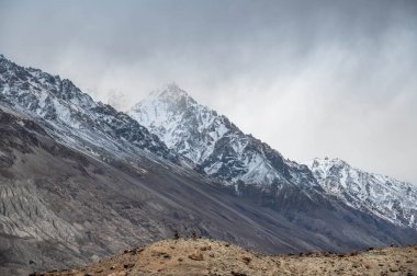 Himalaya dağlarının dramatik bir gökyüzü altında nefes kesici manzarası. Kar zirveleri, engebeli arazi ve el değmemiş vahşi doğa seyahat, macera, meditasyon ve doğa kavramları için mükemmel bir zemin oluşturur..