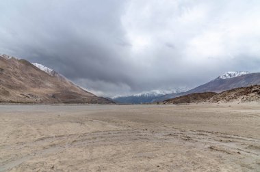 Yarab Tso 'nun manzarası, Hindistan' ın Nubra Vadisi 'ndeki yüksek rakımlı kutsal göl. Ön planda göl kıyısı boyunca beyaz kumlar, görkemli Himalaya dağları ise bulutlu bir gökyüzünün altında yükseliyor..