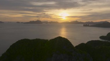 Güneş ufkun altına batar ve suyun üzerinde yumuşak bir kehribar parıltısı yayar. El Nido, Filipinler.