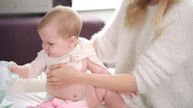 Anne kıyafetlerini bebeğiyle değiştiriyor. Elbise giyen şirin bir bebek.