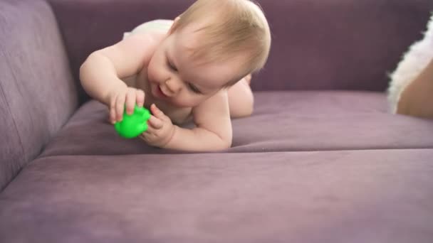 Adorável bebê rastejar na cama violeta. Criança nua em fraldas roendo brinquedo — Vídeo de Stock