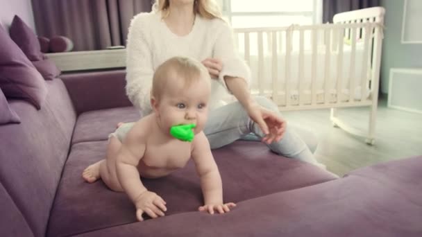 Малыш с игрушкой во рту ползает по дивану. Смешная детская прогулка — стоковое видео