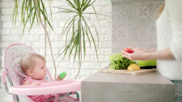Criança bonito olhando para a mãe cozinhar alimentos. Legumes de cozinha feminina — Vídeo de Stock