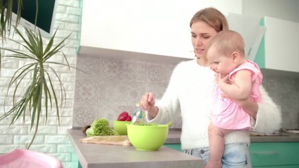 Мама держит ребенка на руках на кухне. Мама с ребенком готовит ужин — стоковое видео