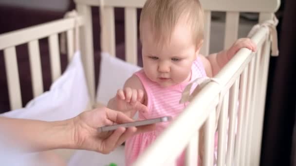 Bayi lucu di tempat tidur bayi menyentuh smartphone. Konsep teknologi bayi — Stok Video