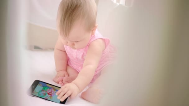 Infant girl with mobile sitting in cot. Baby watching kid cartoon — Stock Video