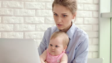 Bilgisayarında bebek olan konsantre bir kadın. İş kadını çalışıyor.