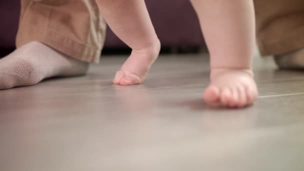 Malé nožičky kráčející po podlaze. Dětské krůčky s podporou otce — Stock video