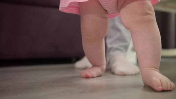 Kleine baby leren lopen op de vloer. Baby doet eerste stappen met vader — Stockvideo