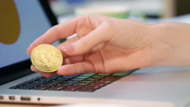 Kvinna hand innehav guld bitcoin mynt nära bärbar dator — Stockvideo