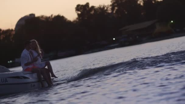 Jóvenes sentados en lancha flotante al atardecer. Pareja de amor en yate — Vídeo de stock