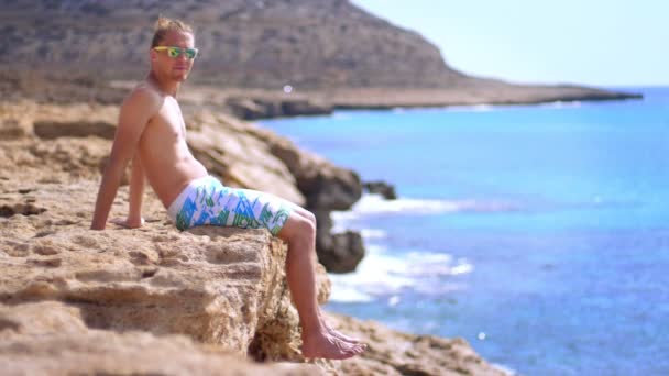 Opalovací muž v uhýbaje sluneční brýle. Stylový muž opalování na skalnatém útesu — Stock video