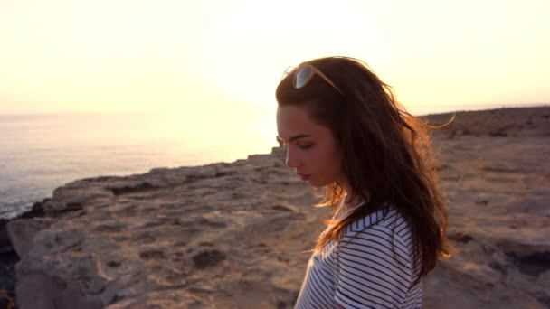 Brunette vrouw genieten van strand zonsondergang. Achteraanzicht van vrouw lopen op rotsachtige strand — Stockvideo