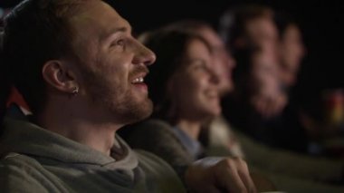 Genç adam film izlerken gülmekten patlamış mısır yemek kulağı küpeli