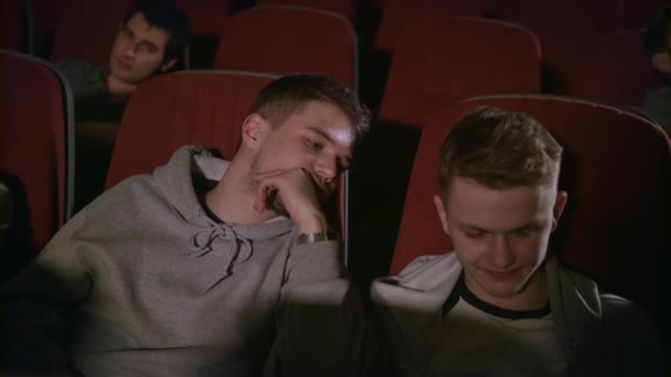 Два хлопці дивляться смартфон у кіно. Друзі розважаються з телефоном в театрі — стокове відео