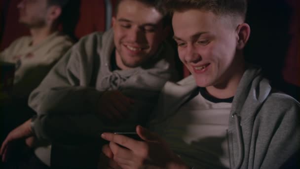 Male friends having fun with mobile phone at cinema. Gay couple using smartphone — Stock Video