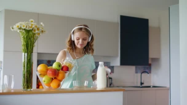 Mooie vrouw luisteren muziek en koken. Mooi meisje dansen — Stockvideo
