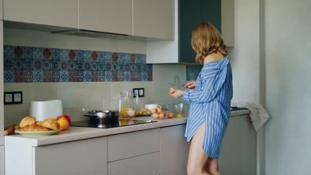 Sexy Mädchen im Hemd kocht Omelette in der Küche. Frühstückszubereitung — Stockvideo