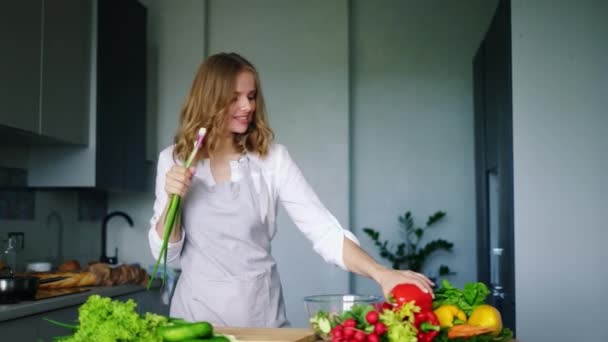 Menina feliz dançando e cantando na cozinha usando pepino como microfone — Vídeo de Stock