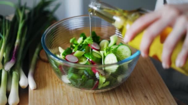 Nő kéz, zuhogó olívaolaj üveg tálba friss tavaszi saláta — Stock videók