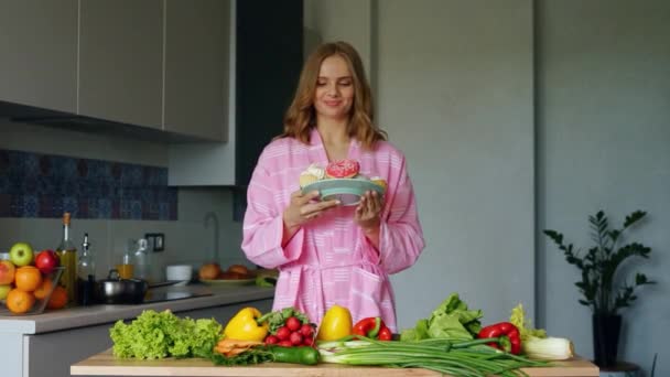 Ragazza sorridente buttando dalla tavola della cucina verdure fresche — Video Stock