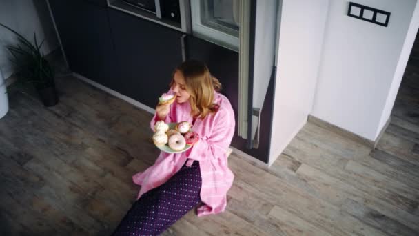 Όμορφη γυναίκα κάθεται στο πάτωμα στην κουζίνα και να τρώει γλυκά. Ικανοποιημένοι κορίτσι — Αρχείο Βίντεο