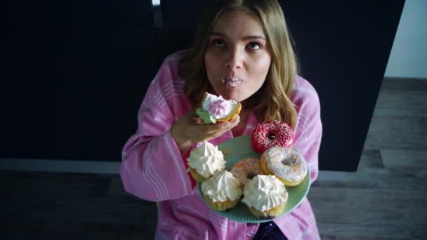 Mulher come demais cupcake doce na mesa da cozinha. Mulher faminta comendo sobremesa — Vídeo de Stock