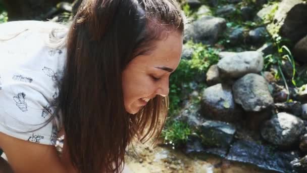 Mladá žena mytí obličeje v pramenité vodě. Horský potok s čistou vodou