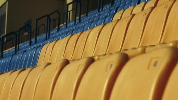 Scaune galbene și albastre goale pe stadionul de fotbal. Închideți rândul de scaune din plastic — Videoclip de stoc