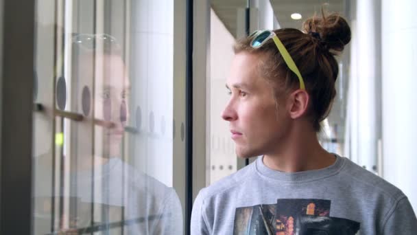 Современный человек смотрит в окно с сопутствующим зрелищем. Парень смотрит в окно — стоковое видео