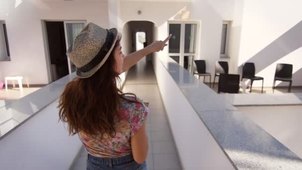 Γυναίκα με καπέλο περπάτημα στο θέρετρο. Μελαχρινή κοπέλα δείχνει ξενοδοχείο. Οδηγός διακοπών — Αρχείο Βίντεο