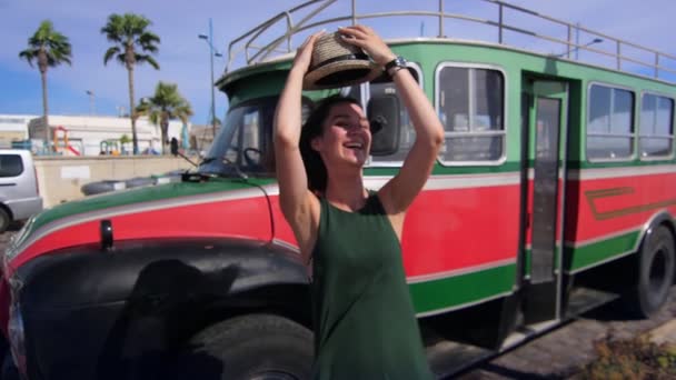 Радостная девушка в шляпе позирует перед камерой на фоне старинного автобуса. Хипстерский образ жизни — стоковое видео