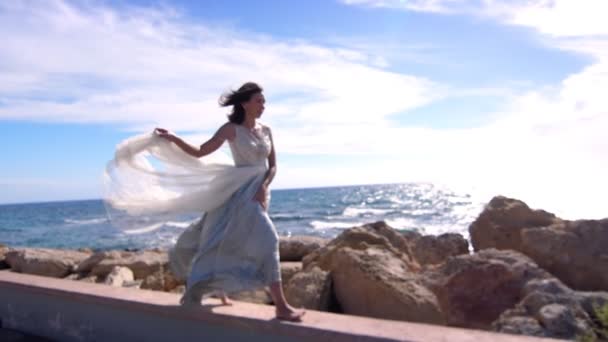 Элегантная женщина в платье ходит по каменному пляжу. Летняя модель наслаждаться морским пейзажем — стоковое видео