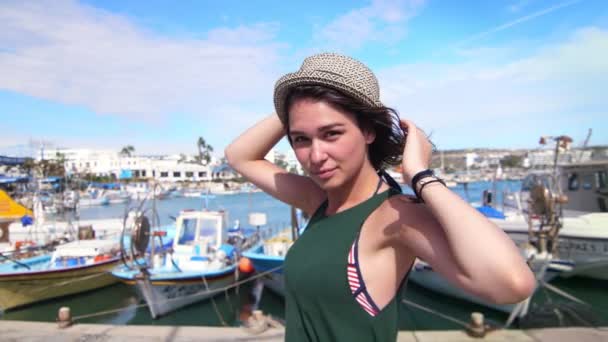 Glad flicka i hatt poserar på kameran under semester på wharf bakgrund — Stockvideo