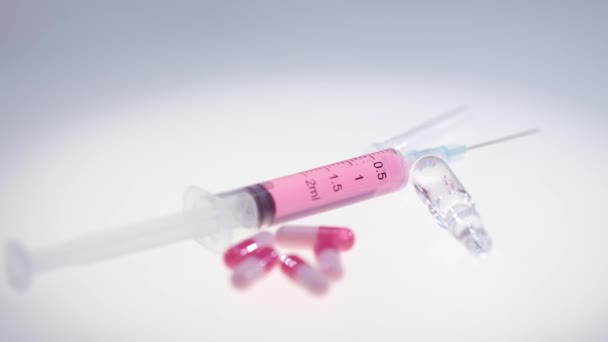 Шприц с розовой жидкостью. Фармацевтические таблетки и ампула из медицинского стекла — стоковое видео