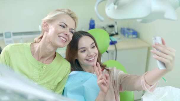 Médico sonriente y paciente tomando selfie en el consultorio del dentista. Mujer mostrando signo v — Vídeo de stock