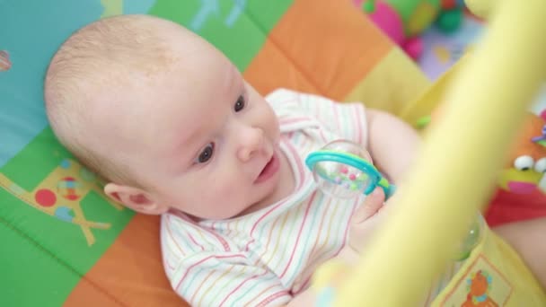 Fröhliches Baby auf buntem Bett liegend. Säugling spielt Spielzeug — Stockvideo