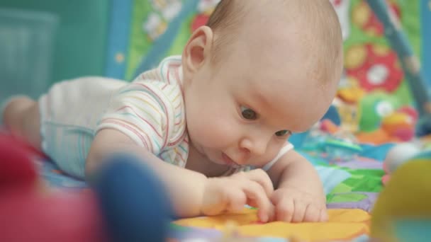 Adorável bebê olhando flor amarela. Close up de criança deitada no tapete colorido — Vídeo de Stock
