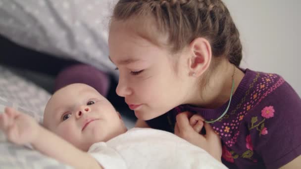Beautiful girl kissing baby lying on sofa. Sister kiss newborn brother — Stock Video