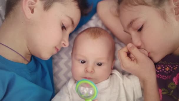 Братья и сёстры с ребёнком в постели. Брат и сестра целуют новорожденного мальчика — стоковое видео