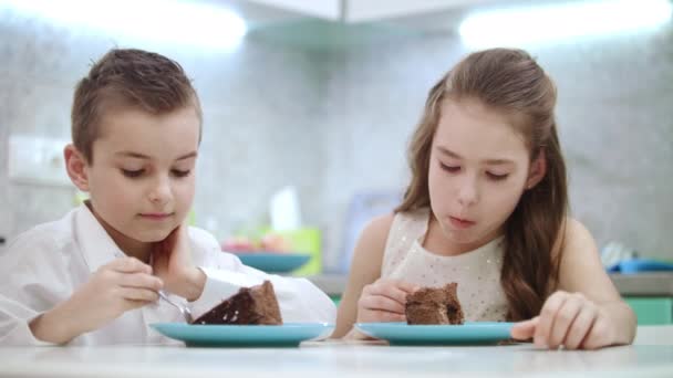 Os irmãos comem bolo de aniversário na cozinha. Crianças comem sobremesa de chocolate em casa — Vídeo de Stock