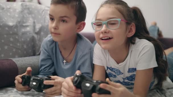 Bambini che giocano ai videogiochi. Bambini sdraiati sul divano con controller in mano — Video Stock